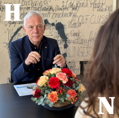 Oberbürgermeister Harry Mergel sitzt an einem Konferenztisch und hört einer ihm gegenüber sitzenden Bürgerin aufmerksam zu.