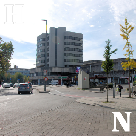 Foto des Wollhausplatzes. Im Hintergrund steht das aktuelle Wollhausgebäude. Darum herum sind die Straße Am Wollhaus und der Busbahnhof zu sehen.