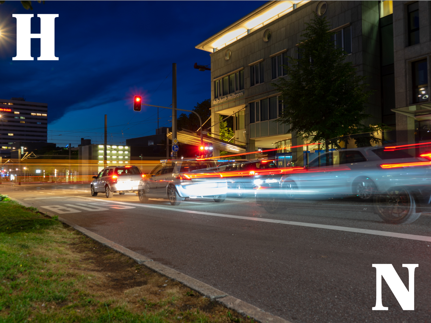Auf dem Foto ist die Heilbronner Allee bei Nacht zu sehen. Verschwommene Autos stehen an einer Ampel vor einem Gebäude. Im Hintergrund ist verschowmmen eine vorbeifahrende Stadtbahn zu sehen.