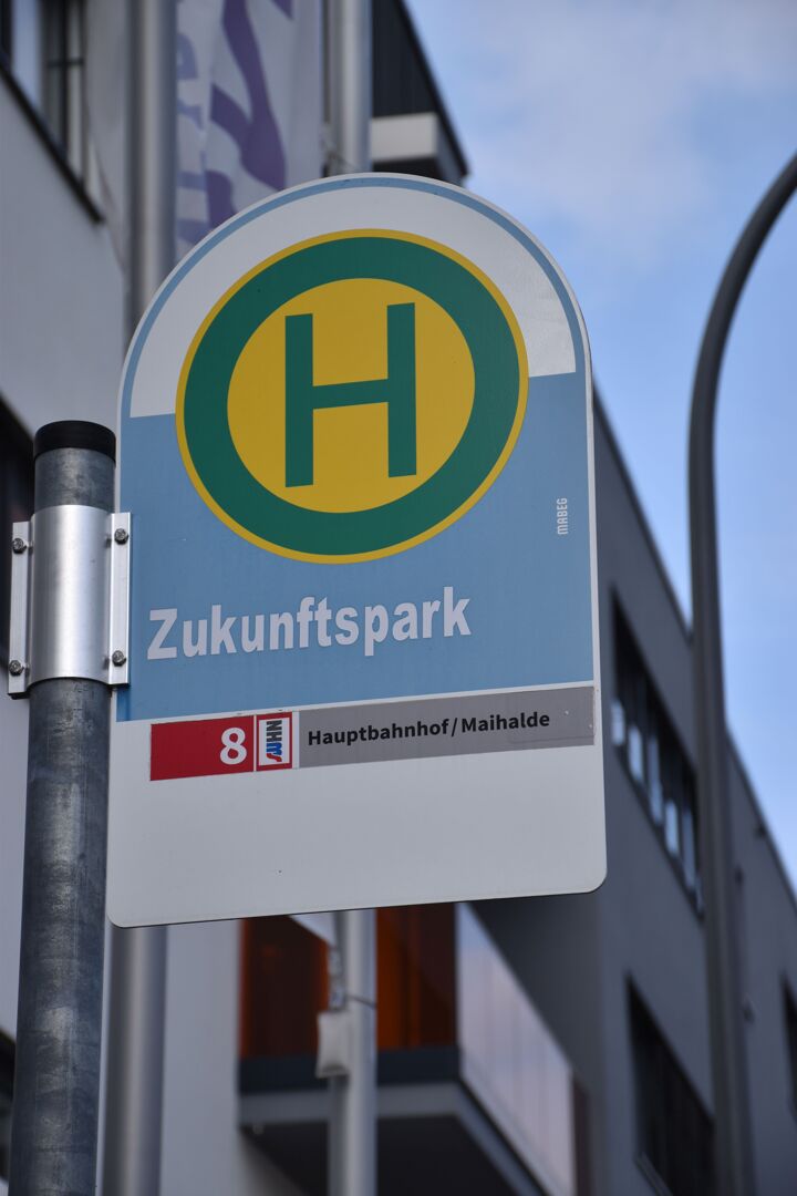 Das Bild zeigt ein Foto von einem Haltestellenschild einer Bushaltestelle. Auf dem Schild ist das Wort "Zukunftspark" aufgedruckt.