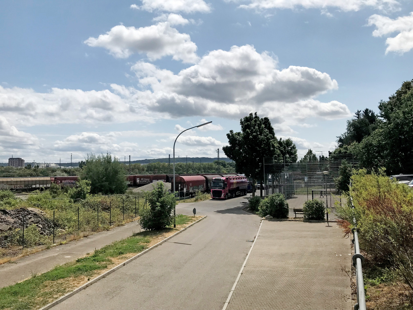 Aktuelles Foto des Teilgebiets, das in den zweiten Bauabschnitt fällt. Zu sehen ist eine verwachsene Brachfläche. Parallel laufen Bahngleise mit Güterzügen entlang.